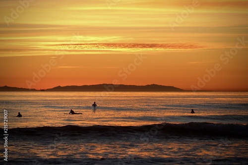 bright orange sunset over the ocean showing silhouettes of surfers waiting for waves 