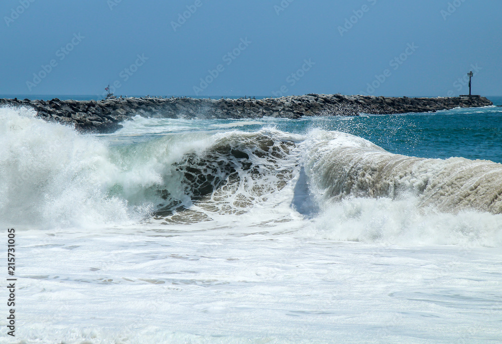 waves crashing on the shore with a rock jetty in the background 