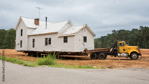 An old white house being transported on the back of a truck.