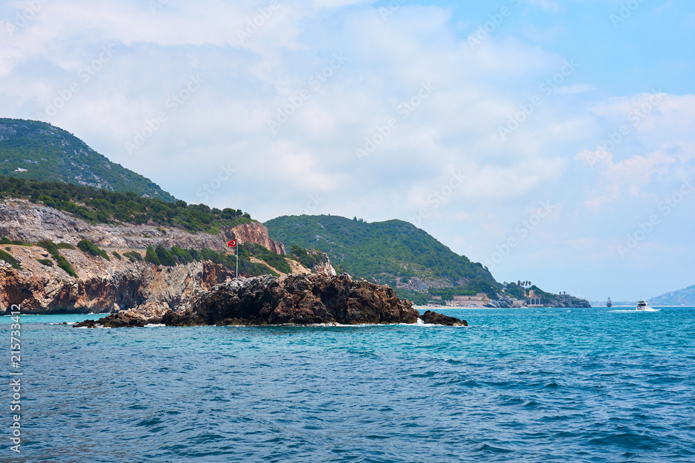  Flag of Turkey on rocks in sea coast of Alanya. Cloudy blue sky. 