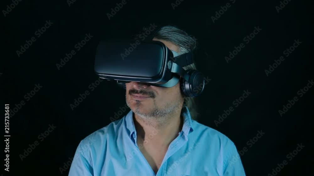 Close up shot of an adult man wearing virtual reality glasses at black background - looking around via virtual reality interface. Slow motion shot. Close up shot of an adult man wearing virtual reality glasses at black background - looking around via virtual reality interface. Slow motion shot.
