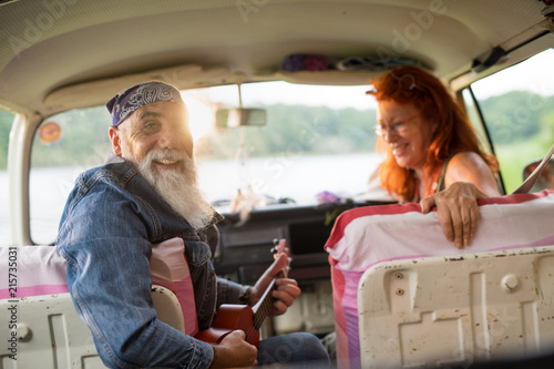 An old hipster couple sitting in a van, the man playing ukulele  © jackfrog