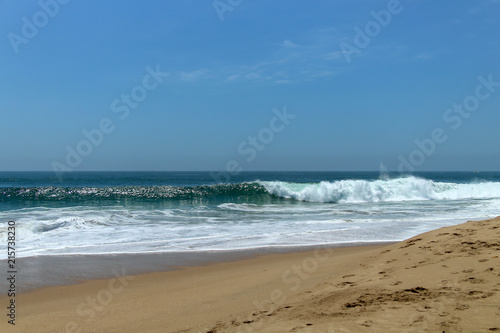 wave crashing at the beach with sailboat in the background 