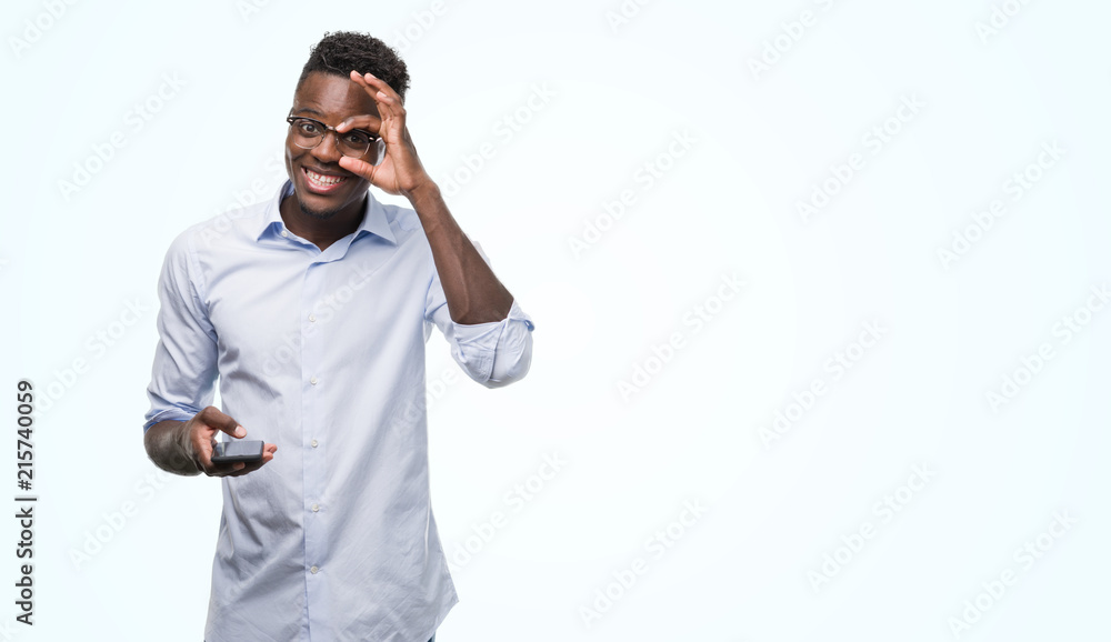 Young african american man using smartphone with happy face smiling doing ok sign with hand on eye looking through fingers Young african american man using smartphone with happy face smiling doing ok sign with hand on eye looking through fingers