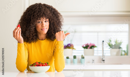 African american woman eating strawberries at home pointing with hand and finger up with happy face smiling