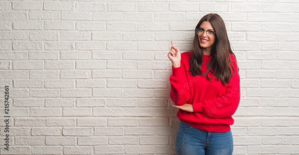 Young brunette woman standing over white brick wall pointing finger up with successful idea. Exited and happy. Number one. Young brunette woman standing over white brick wall pointing finger up with successful idea. Exited and happy. Number one.