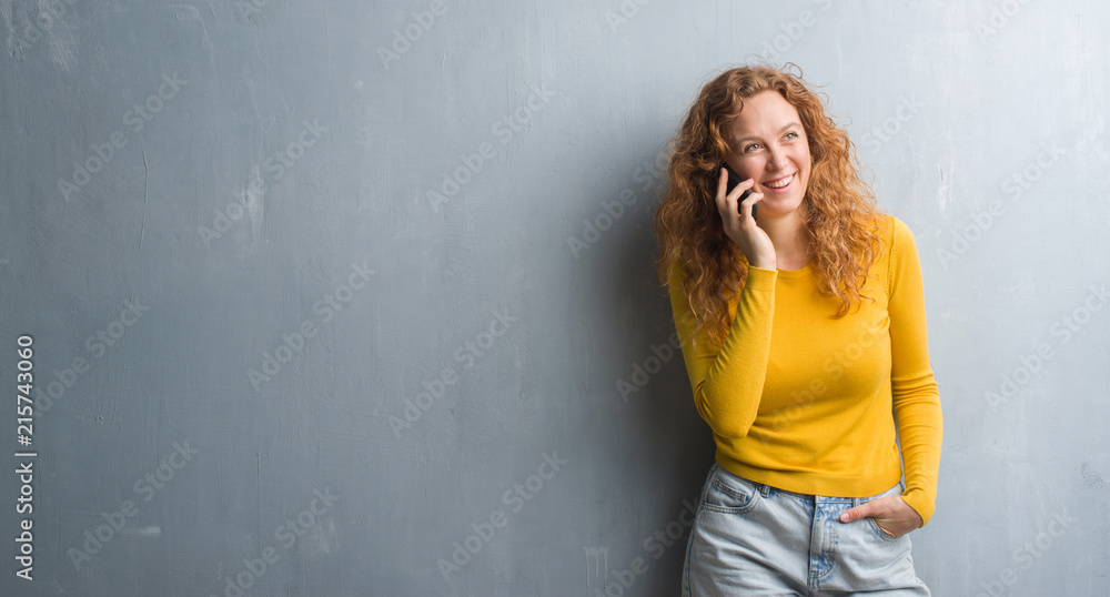 Young redhead woman over grey grunge wall talking on the phone with a happy face standing and smiling with a confident smile showing teeth