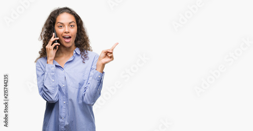 Young hispanic woman using smartphone very happy pointing with hand and finger to the side