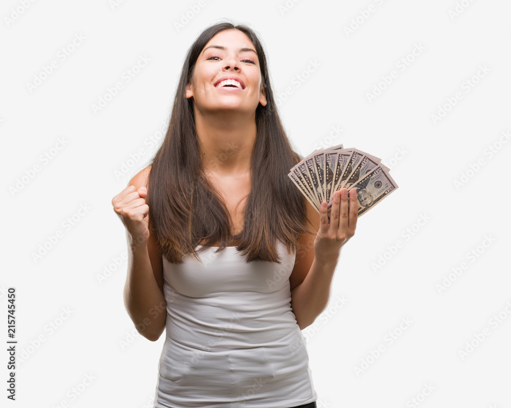 Young hispanic woman holding dollars screaming proud and celebrating victory and success very excited, cheering emotion Young hispanic woman holding dollars screaming proud and celebrating victory and success very excited, cheering emotion