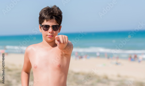 Young child on holidays at the beach pointing with finger to the camera and to you, hand sign, positive and confident gesture from the front