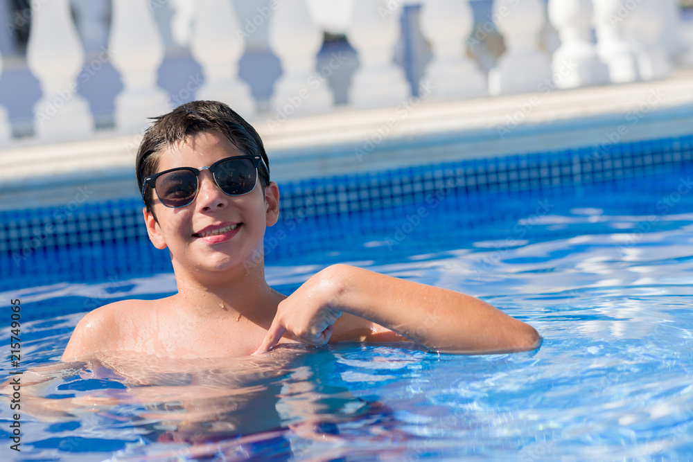 Young child on holiday at the swimming pool by the beach with surprise face pointing finger to himself