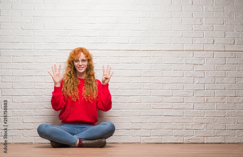 Young redhead woman sitting over brick wall showing and pointing up with fingers number nine while smiling confident and happy. Young redhead woman sitting over brick wall showing and pointing up with fingers number nine while smiling confident and happy.