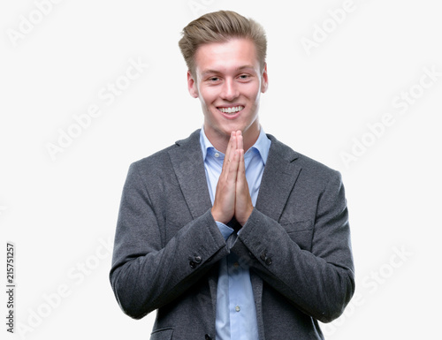 Young handsome blond business man praying with hands together asking for forgiveness smiling confident.