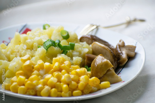 Fried potatoes with cepes and corn in a plate on the table. Fried potatoes with pickled mushrooms and corn.