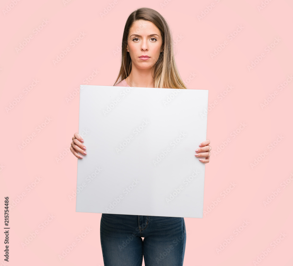 Beautiful young woman holding advertising banner with a confident expression on smart face thinking serious