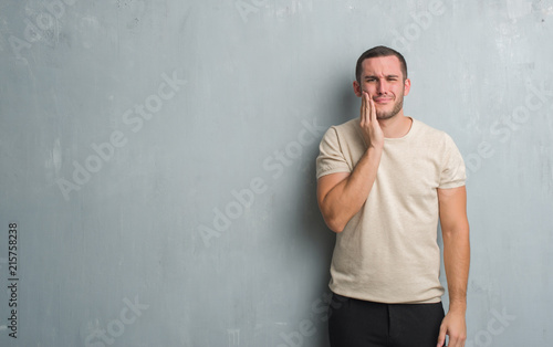 Young caucasian man over grey grunge wall touching mouth with hand with painful expression because of toothache or dental illness on teeth. Dentist concept. © Krakenimages.com