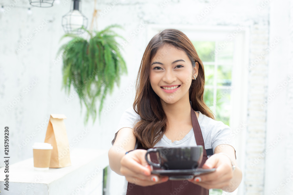 Asian Women Barista smiling and looking to camera in coffee shop counter. Barista female holding coffee cup at cafe. Working woman small business owner or sme concept. Asian Women Barista smiling and looking to camera in coffee shop counter. Barista female holding coffee cup at cafe. Working woman small business owner or sme concept.