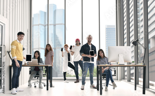 Group of businesspersons each holding an electronic device or gadget looking happy and joyful in a casual office.