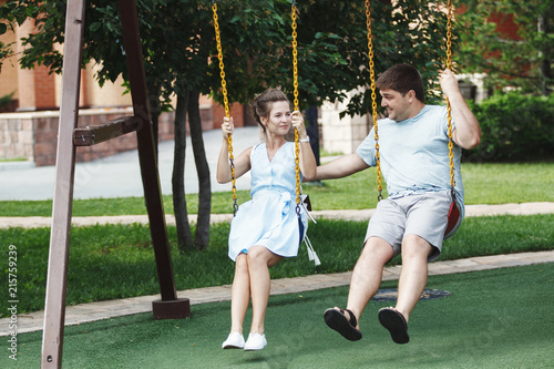 Young cute couple woman and a man in a family look ride on a swing in the playground. photo