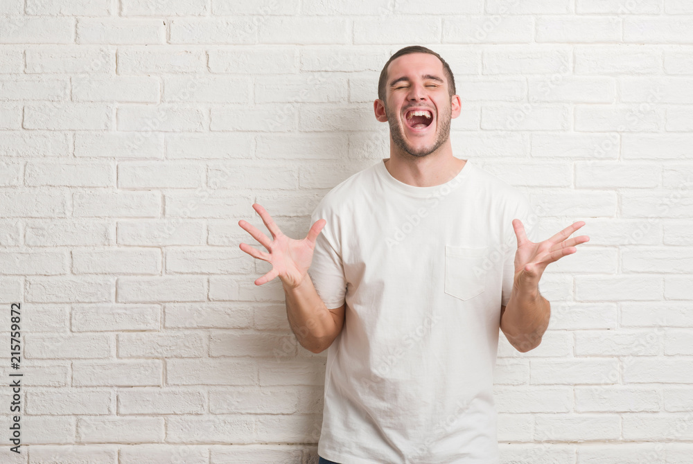 Young caucasian man standing over white brick wall with hand on chin thinking about question, pensive expression. Smiling with thoughtful face. Doubt concept. Young caucasian man standing over white brick wall with hand on chin thinking about question, pensive expression. Smiling with thoughtful face. Doubt concept.