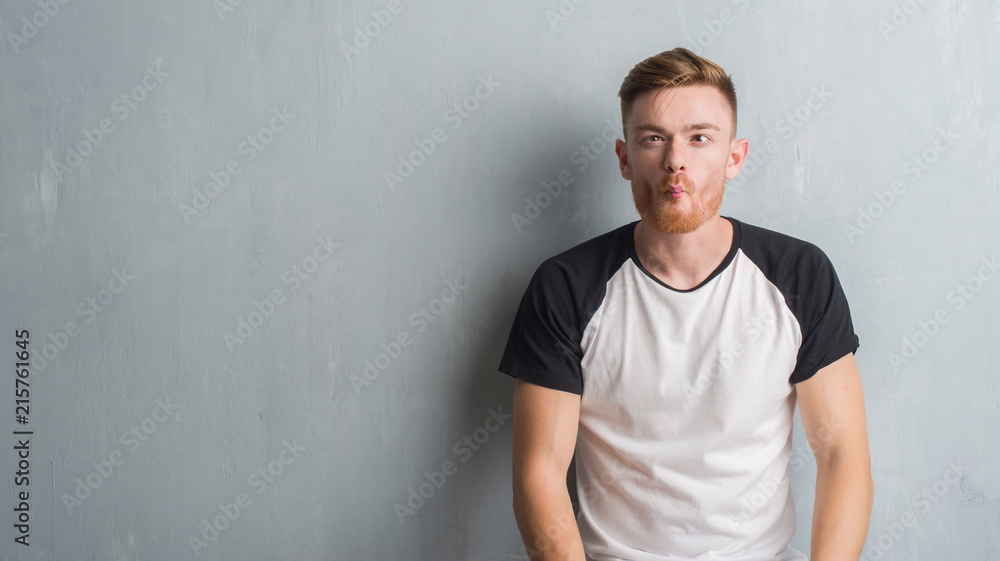 Young redhead man over grey grunge wall making fish face with lips, crazy and comical gesture. Funny expression. Young redhead man over grey grunge wall making fish face with lips, crazy and comical gesture. Funny expression.