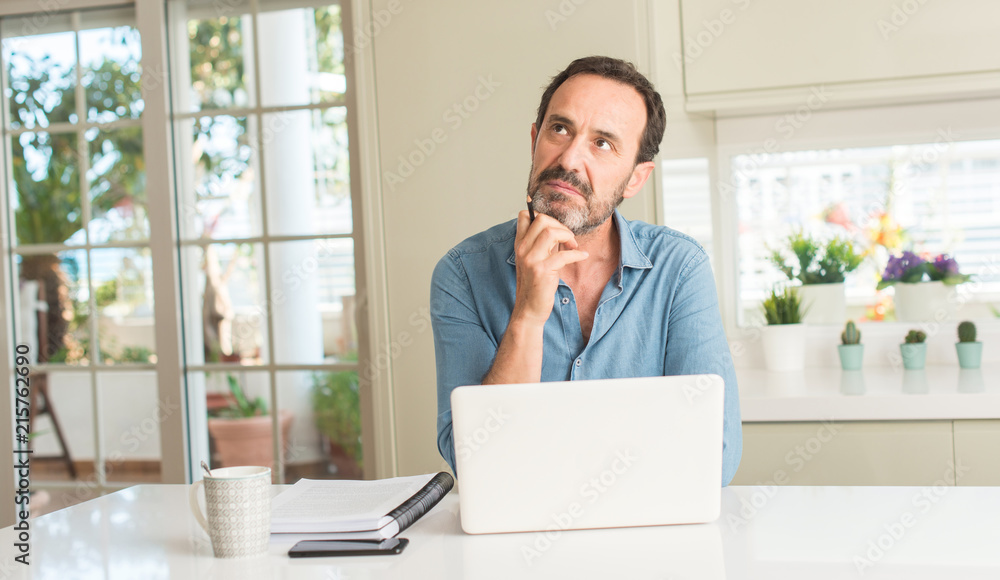 Middle age man using laptop at home serious face thinking about question, very confused idea Middle age man using laptop at home serious face thinking about question, very confused idea
