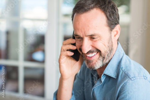 Middle age man using smartphone with a happy face standing and smiling with a confident smile showing teeth