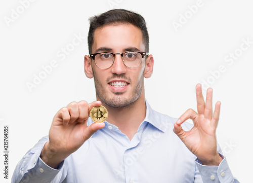 Handsome young man holding bitcoin doing ok sign with fingers, excellent symbol