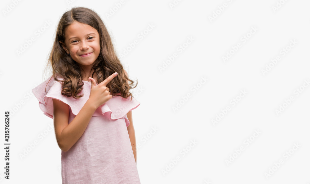 Brunette hispanic girl wearing pink dress cheerful with a smile of face pointing with hand and finger up to the side with happy and natural expression on face looking at the camera. Brunette hispanic girl wearing pink dress cheerful with a smile of face pointing with hand and finger up to the side with happy and natural expression on face looking at the camera.