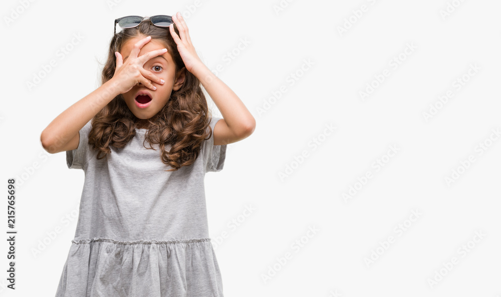 Brunette hispanic girl wearing sunglasses peeking in shock covering face and eyes with hand, looking through fingers with embarrassed expression. Brunette hispanic girl wearing sunglasses peeking in shock covering face and eyes with hand, looking through fingers with embarrassed expression.