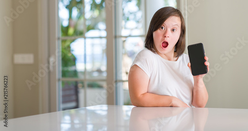 Down syndrome woman at home using smartphone scared in shock with a surprise face, afraid and excited with fear expression