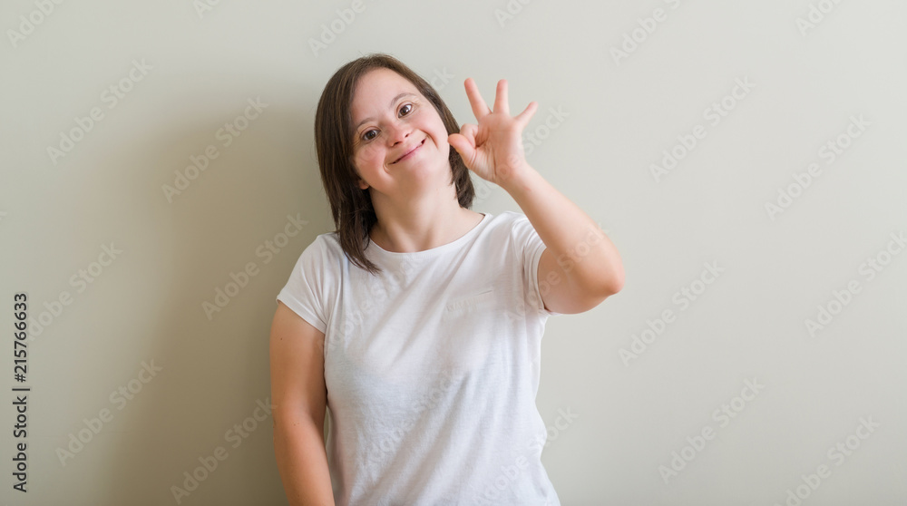 Down syndrome woman standing over wall smiling positive doing ok sign with hand and fingers. Successful expression. Down syndrome woman standing over wall smiling positive doing ok sign with hand and fingers. Successful expression.