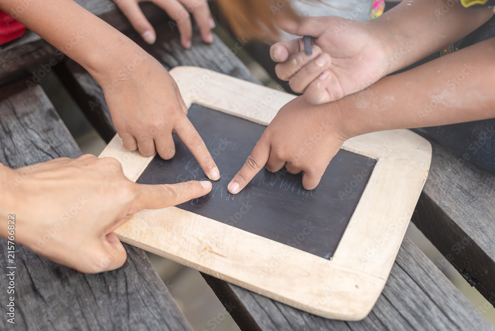 Children enjoy writing and drawing using a blackboard outdoor. Mother teach here little children to write on blackboard outdoor. Poor children using a small board for writing in countryside. Children enjoy writing and drawing using a blackboard outdoor. Mother teach here little children to write on blackboard outdoor. Poor children using a small board for writing in countryside.