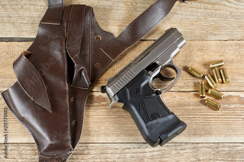 pistol with ammunition and shoulder holster on a wood background