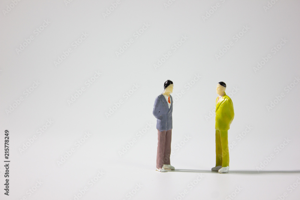 Two miniature businessman talking on gray background.