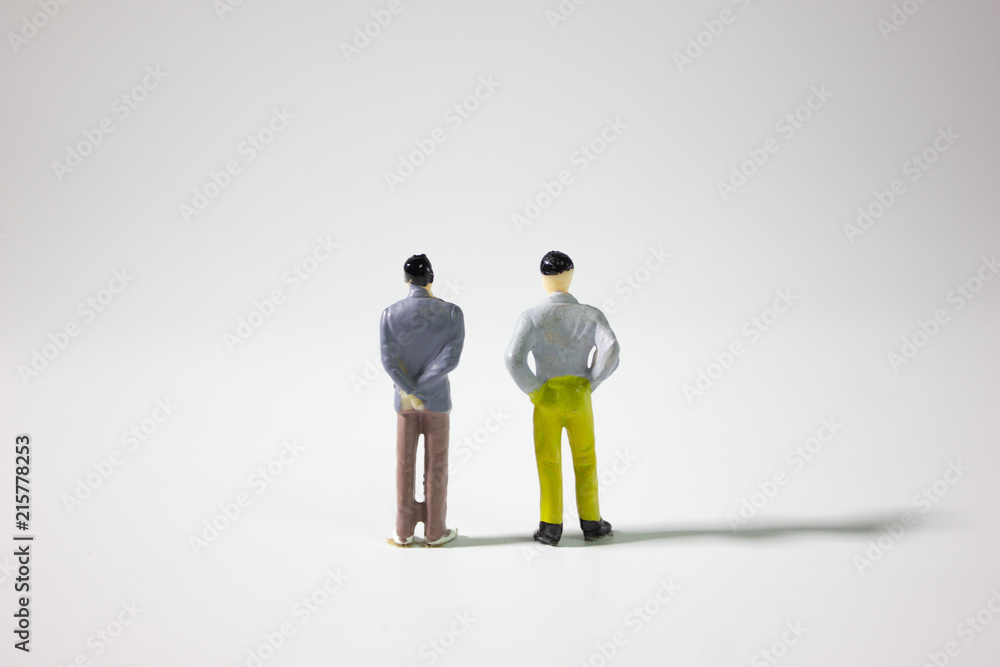 Two miniature businessman on gray background closeup.