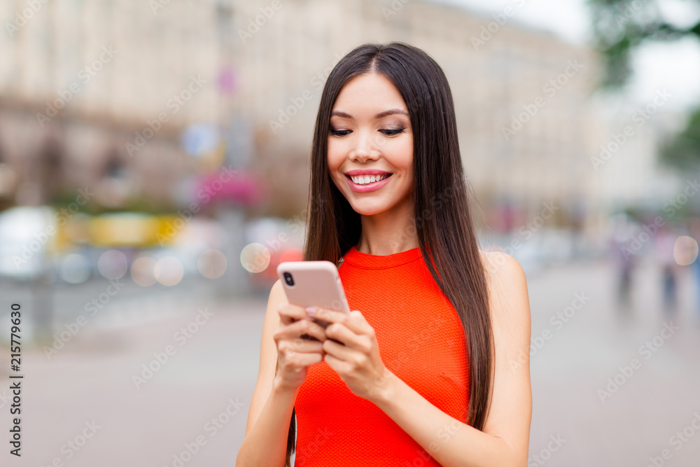 Portrait of lovely and cute asian girl writes a message to friends about meet and walk around the city on a sunny summer day against a blurred background of cityscape Portrait of lovely and cute asian girl writes a message to friends about meet and walk around the city on a sunny summer day against a blurred background of cityscape