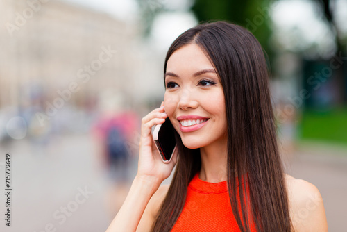Portrait of confident and calm Asian girl who speaks on a smartphone against a backdrop of a little blurry city