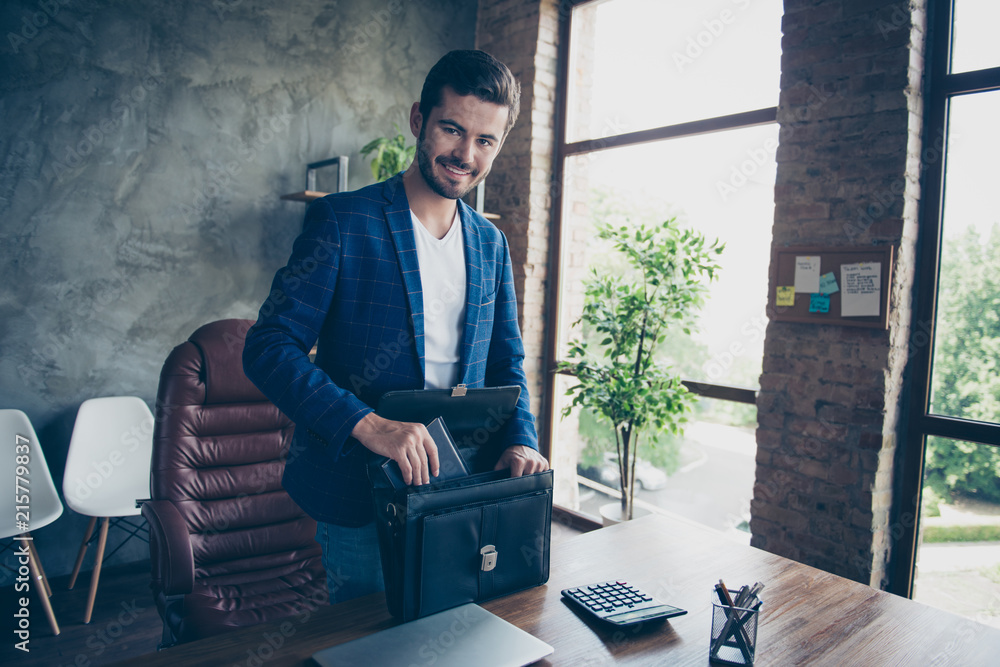 Attractive handsome young brunet bearded executive worker smiling cheerful man, accountant at workstation workplace. Finishing, collecting things in breif-case after work day goes home