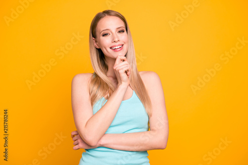 Portrait of charming blonde girl looks into the camera holding her hand to the chin isolated on bright yellow background