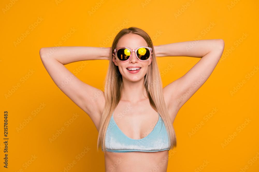 Attractive nice cute straight-haired smiling blonde caucasian girl, wearing blue swimsuit and color sun glasses, having rest, on trip vacation. Isolated over yellow background Attractive nice cute straight-haired smiling blonde caucasian girl, wearing blue swimsuit and color sun glasses, having rest, on trip vacation. Isolated over yellow background