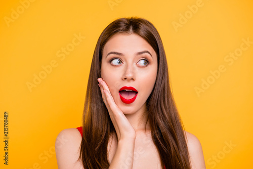 Summer sale?! Close up portrait of coquettish and charming brunette with red lipstick on her lips tells a gossip putting her hand to her cheek isolated on bright yellow background
