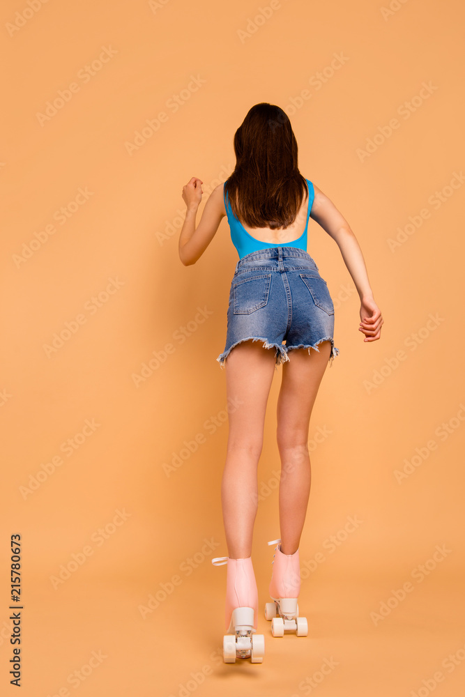 Full-size rear behind view vertical portrait of brunette girl who leaves ahead on the roller skates isolated on pastel peach background Full-size rear behind view vertical portrait of brunette girl who leaves ahead on the roller skates isolated on pastel peach background