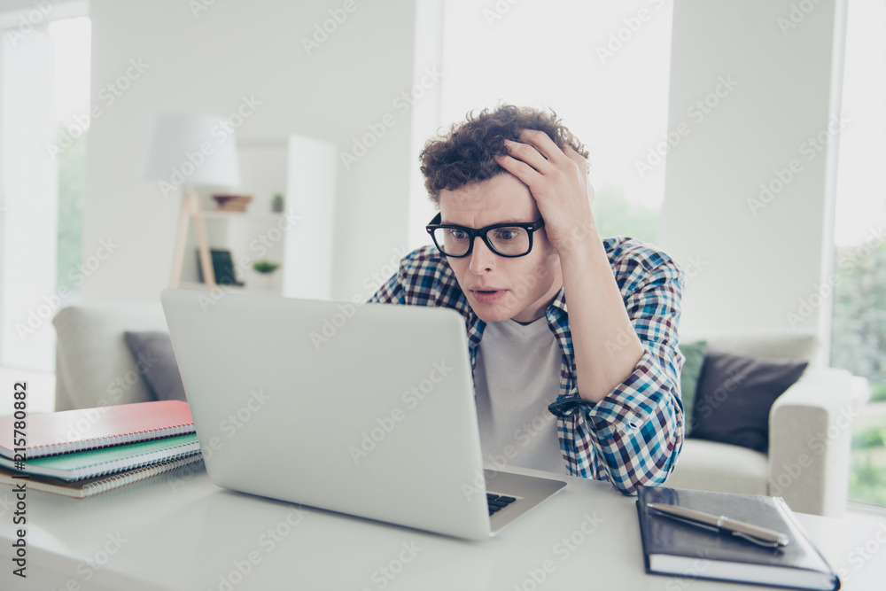 Handsome curly-haired serious young guy student, wearing casual, checkered shirt, looking at laptop, starting online-business, freelance Handsome curly-haired serious young guy student, wearing casual, checkered shirt, looking at laptop, starting online-business, freelance