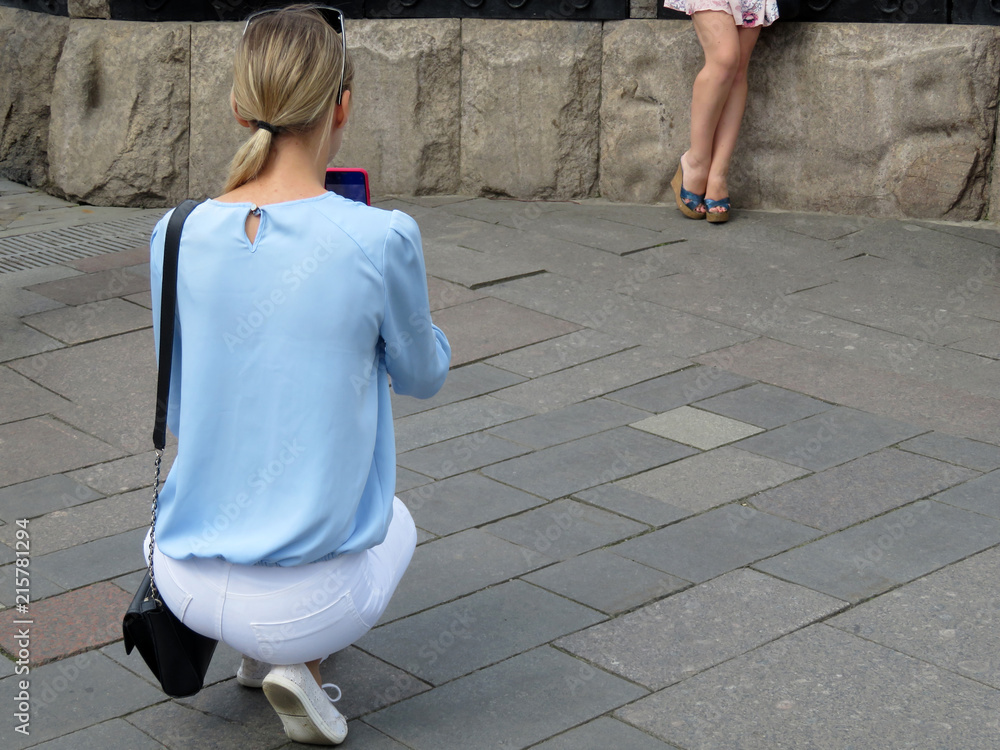 Young woman takes pictures of a girl in short dress on a smartphone camera.  Photo shoot in a summer city, amateur mobile photographing Stock Photo |  Adobe Stock