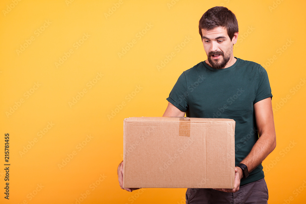 Attractive happy smiling delivery man with a cartboard box in his hands on yellow background in studio Attractive happy smiling delivery man with a cartboard box in his hands on yellow background in studio
