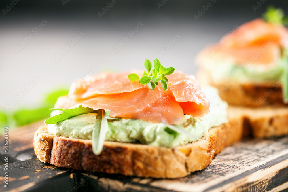 Green cream cheese, salmon and arugula sandwich on a wooden board. Smorrebrod Green cream cheese, salmon and arugula sandwich on a wooden board. Smorrebrod