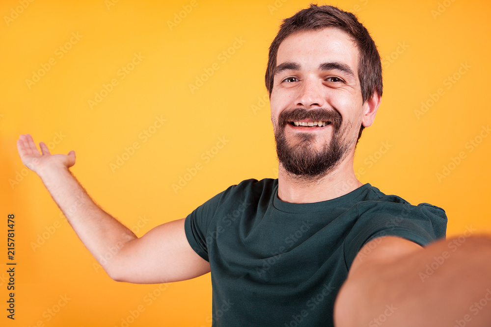 Cool smiling handsome guy smiling at the camera while taking a selfie on yellow background in studio. Recreation and lifestyle Cool smiling handsome guy smiling at the camera while taking a selfie on yellow background in studio. Recreation and lifestyle