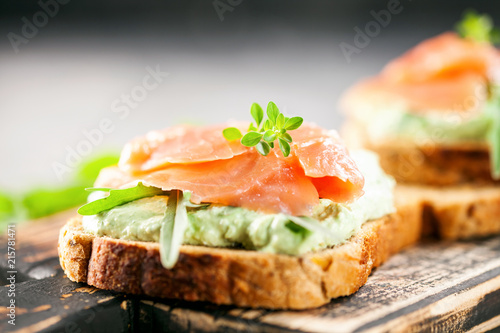 Green cream cheese, salmon and arugula sandwich on a wooden board. Smorrebrod