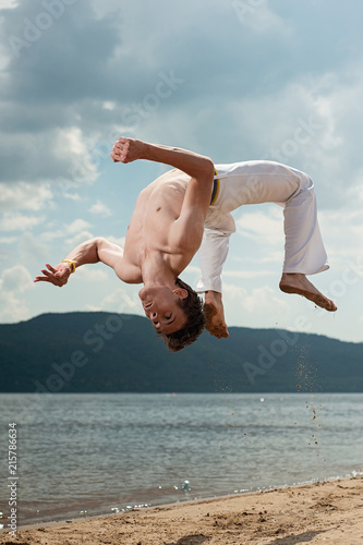 Fotografie Acrobat performs an acrobatic trick, somersault on the beach.